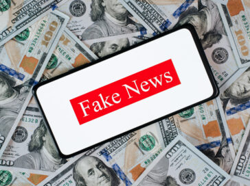 Celular com a frase fake news, em cima de uma pilha de dinheiro