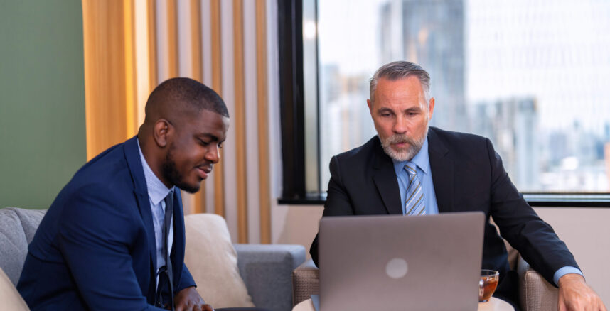 Two businessmen sitting on sofa working discuss on financial forecast together on laptop information pedro braggio mentor financeiro empresarial em 2025 scaled