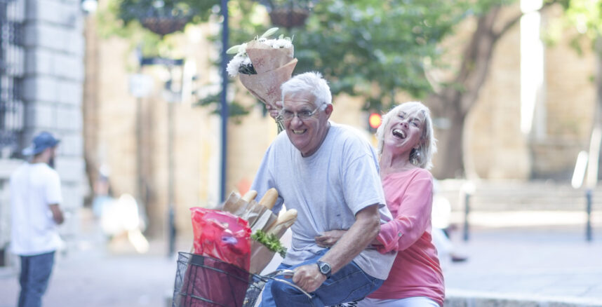 Senior man and woman holding up bouquet cycling in city pedro braggio planejamento financeiro para idosos scaled