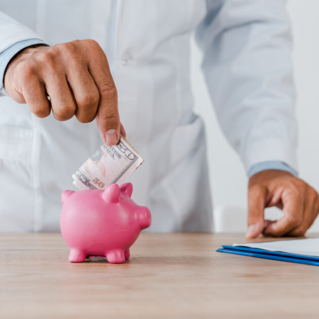 Por Que Contratar um Consultor Financeiro Especializado em Clínicas médicas em 2025? 2 Médico guardando dinheiro no cofrinho, após sessão com consultor financeiro especializado em clínicas médicas