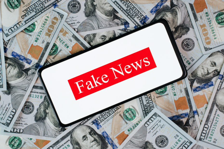 Celular com a frase fake news, em cima de uma pilha de dinheiro