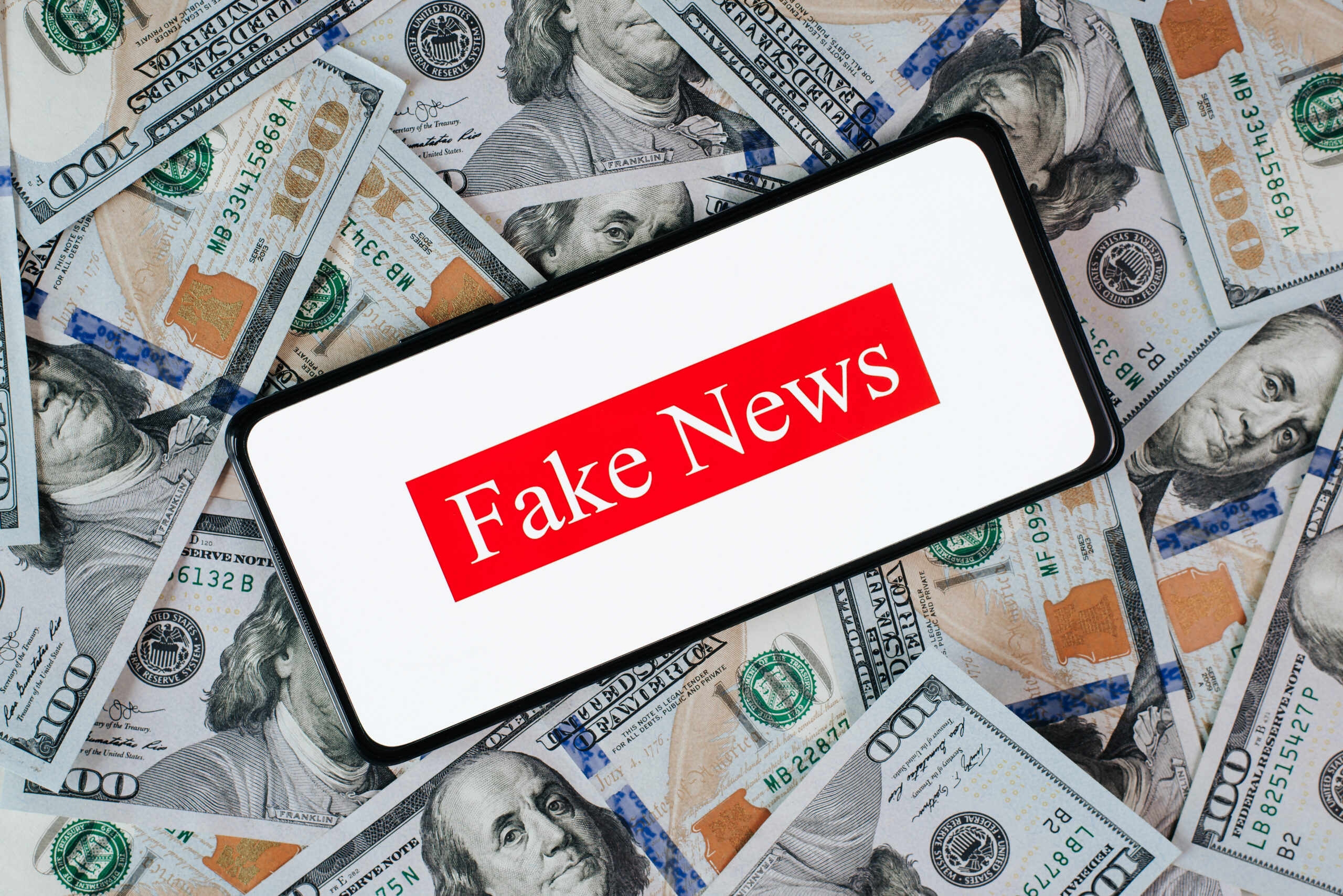 Celular com a frase fake news, em cima de uma pilha de dinheiro